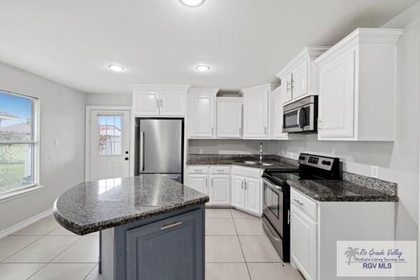 kitchen featuring light tile patterned floors, stainless steel appliances, a sink, white cabinetry, and a center island