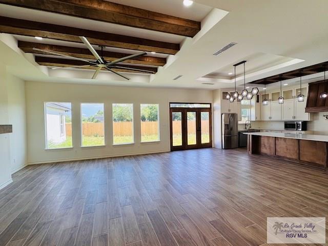 16602 Napper Ln, Primera, TX 78552 - unfurnished living room with dark wood finished floors, a tray ceiling, beam ceiling, baseboards, and a chandelier