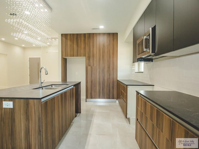 kitchen with an inviting chandelier, a center island with sink, sink, decorative backsplash, and light tile patterned floors