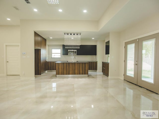 kitchen with modern cabinets, marble finish floor, a kitchen island with sink, stainless steel microwave, and french doors