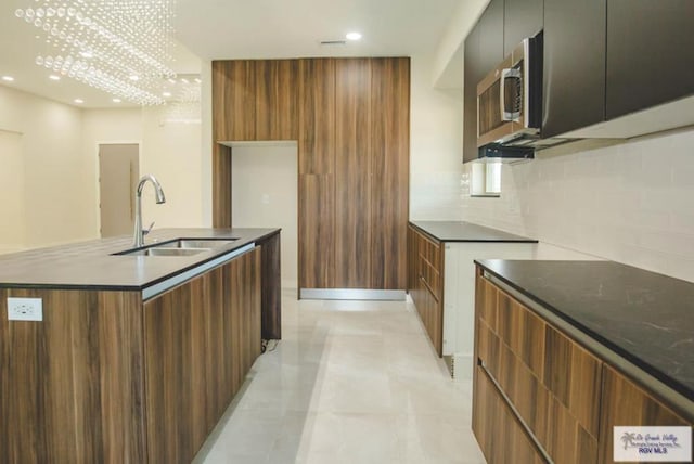 kitchen with an inviting chandelier, sink, decorative backsplash, light tile patterned floors, and an island with sink