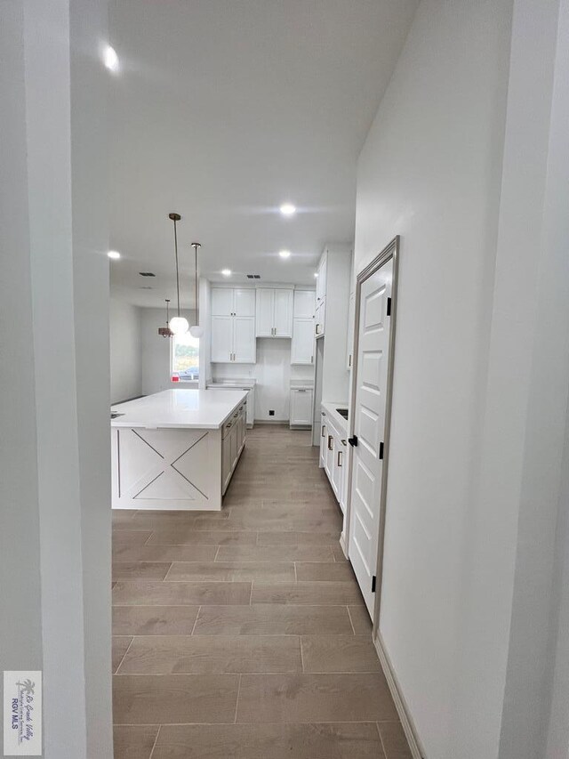 kitchen with light hardwood / wood-style floors, white cabinets, hanging light fixtures, and a kitchen island