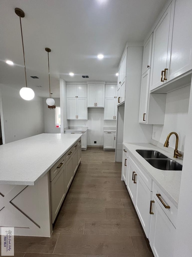 kitchen with pendant lighting, dark wood-type flooring, white cabinets, sink, and light stone countertops