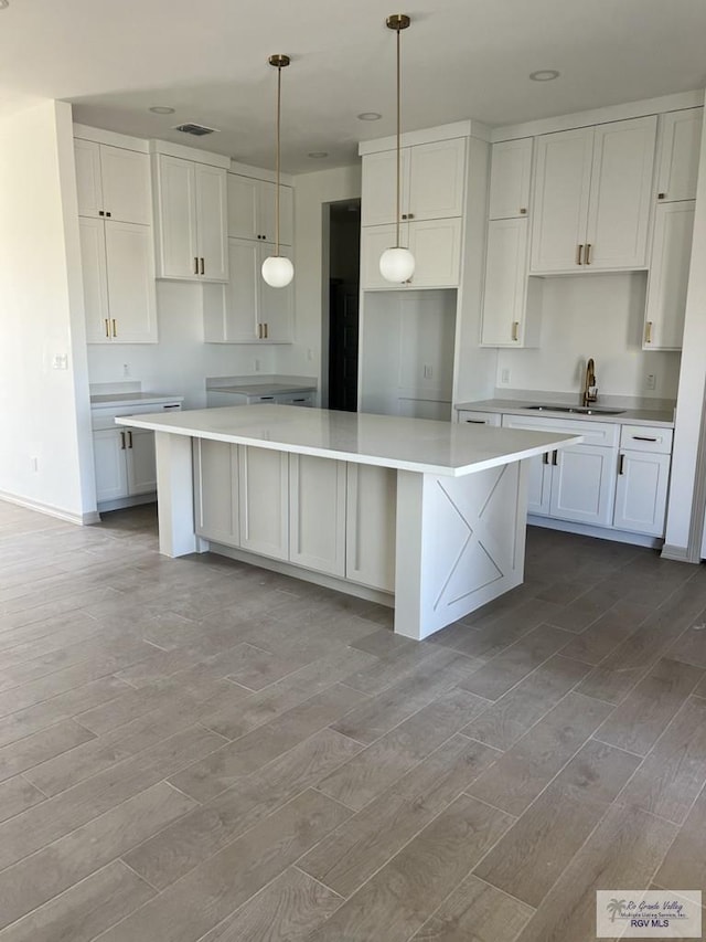 kitchen with white cabinetry, sink, a kitchen island, and light wood-type flooring