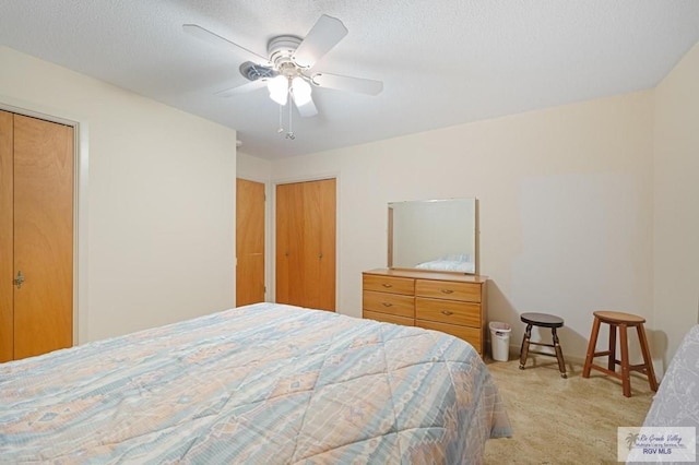 bedroom with a textured ceiling, two closets, ceiling fan, and carpet floors