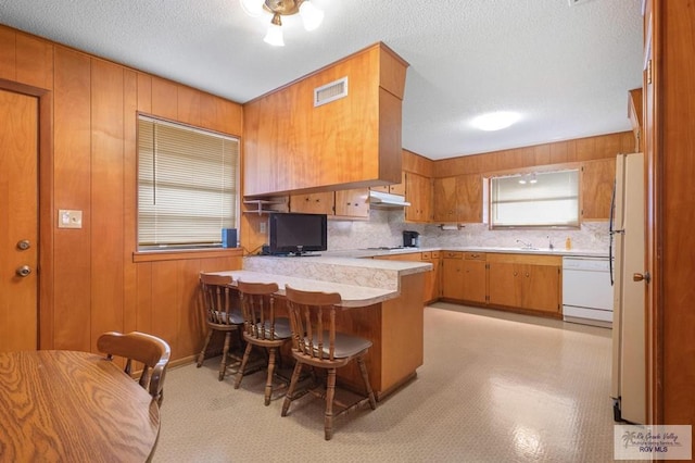 kitchen with visible vents, light countertops, a peninsula, brown cabinetry, and white appliances