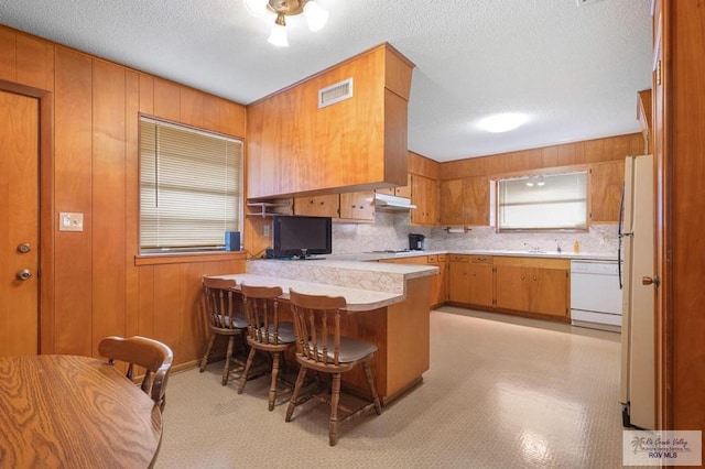 7969 Fm 2099, Lyford, TX 78580 - kitchen with white appliances, a peninsula, under cabinet range hood, brown cabinets, and light countertops