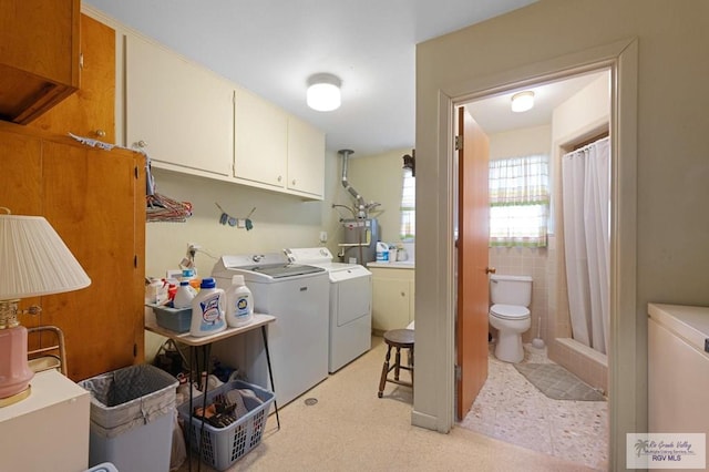 laundry area with electric water heater, washer and clothes dryer, light floors, cabinet space, and tile walls