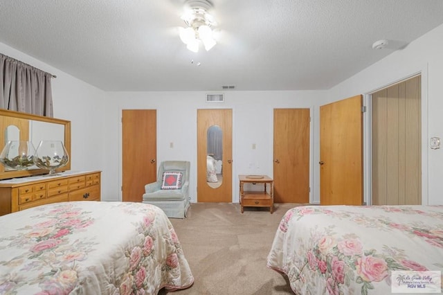 bedroom featuring visible vents, light carpet, a textured ceiling, and multiple closets