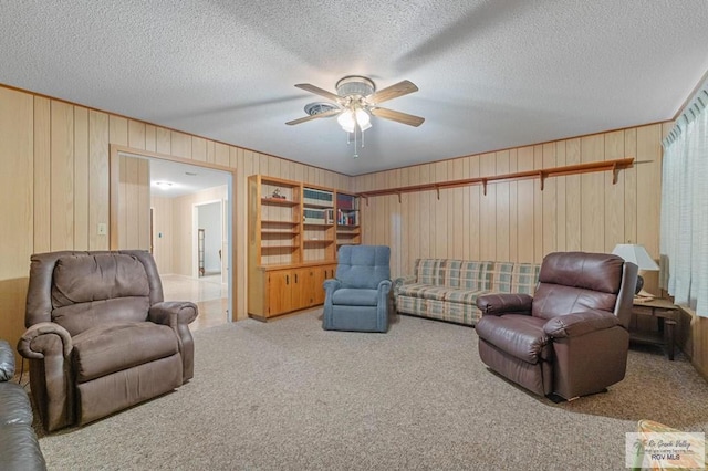 carpeted living room with ceiling fan, wooden walls, and a textured ceiling