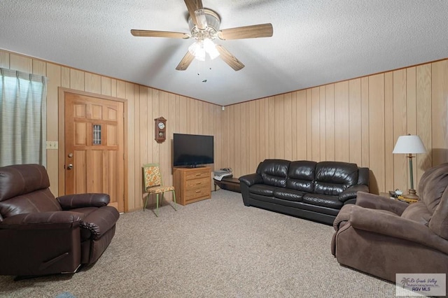 living area with a ceiling fan, carpet, wood walls, and a textured ceiling