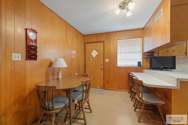 dining space featuring wooden walls, light carpet, visible vents, and a textured ceiling