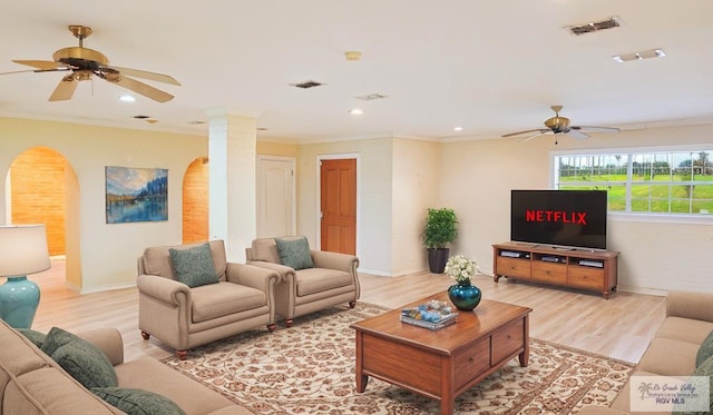 living room featuring crown molding, light hardwood / wood-style floors, ceiling fan, and ornate columns