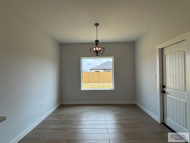 unfurnished dining area featuring wood tiled floor, a chandelier, and baseboards