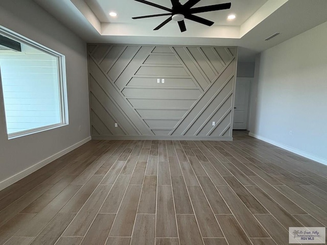 interior space with ceiling fan, a raised ceiling, visible vents, baseboards, and wood finished floors