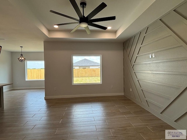 spare room featuring baseboards, ceiling fan, dark wood-style flooring, and a tray ceiling