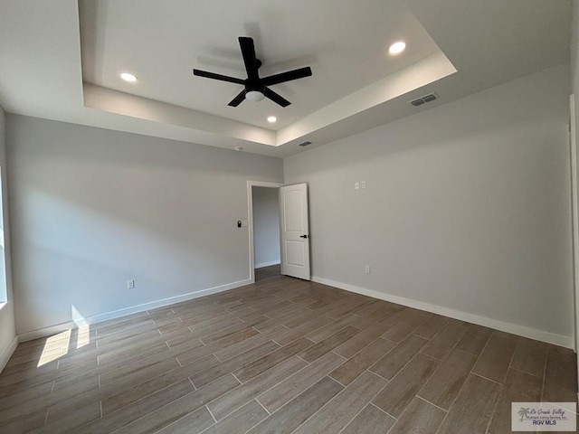 unfurnished room with wood tiled floor, visible vents, a ceiling fan, and a tray ceiling