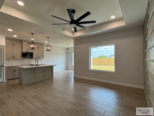 kitchen with tasteful backsplash, light countertops, a sink, black microwave, and open floor plan
