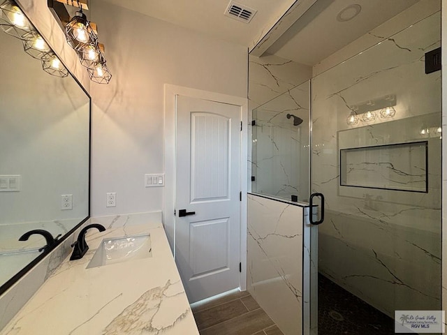 bathroom with a marble finish shower, visible vents, wood finished floors, and vanity