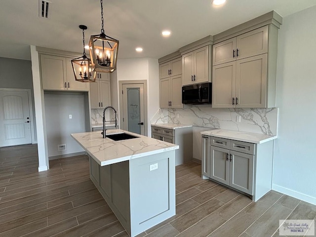 kitchen with gray cabinets, black microwave, wood finished floors, and a sink