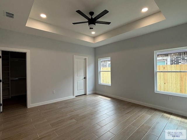 unfurnished bedroom with recessed lighting, wood tiled floor, a raised ceiling, visible vents, and baseboards