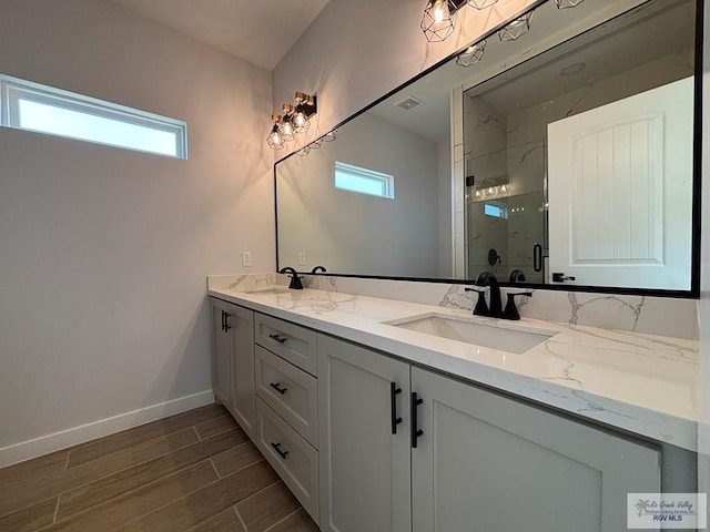 full bathroom with wood finished floors, a wealth of natural light, double vanity, a sink, and a marble finish shower