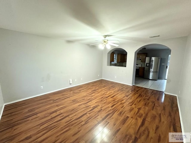 unfurnished living room featuring arched walkways, ceiling fan, visible vents, baseboards, and light wood finished floors