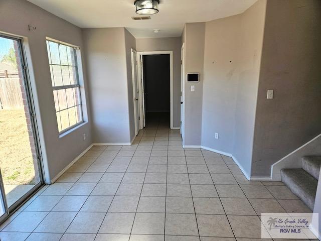 unfurnished room with stairs, a wealth of natural light, and light tile patterned flooring