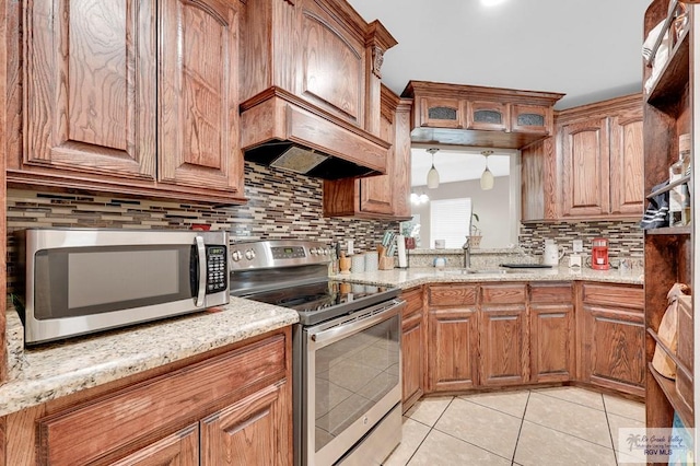kitchen with light tile patterned floors, brown cabinets, appliances with stainless steel finishes, and decorative backsplash