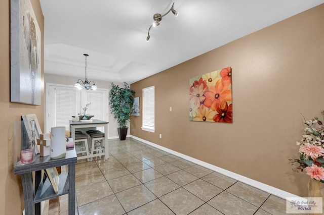 hall featuring baseboards, a chandelier, light tile patterned flooring, and a tray ceiling