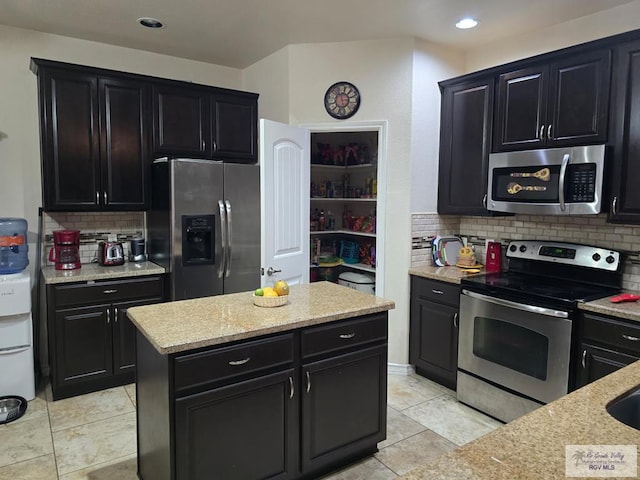 kitchen with light tile patterned floors, stainless steel appliances, dark cabinetry, and tasteful backsplash