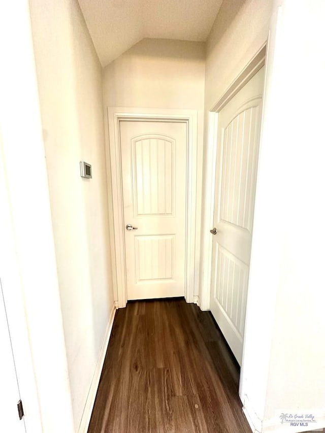 corridor with vaulted ceiling, a textured ceiling, and dark hardwood / wood-style floors