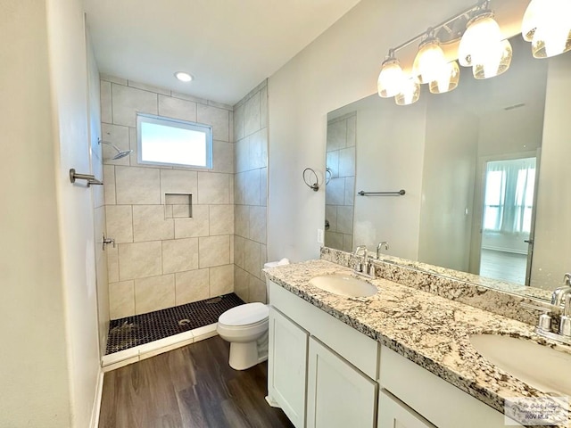 bathroom featuring toilet, hardwood / wood-style flooring, a tile shower, and vanity