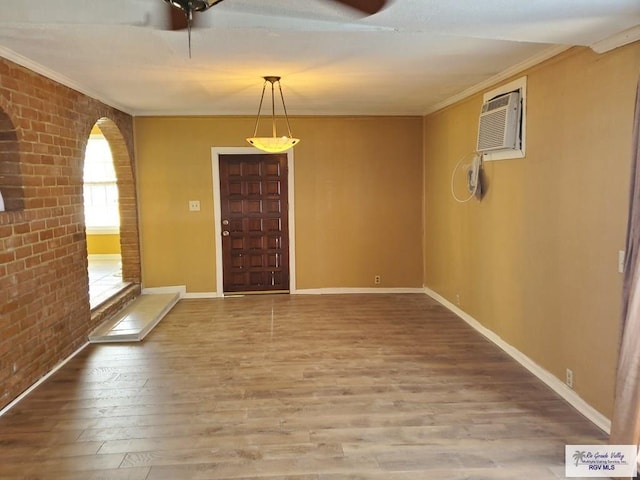 interior space with wood finished floors, baseboards, brick wall, a wall mounted AC, and ornamental molding