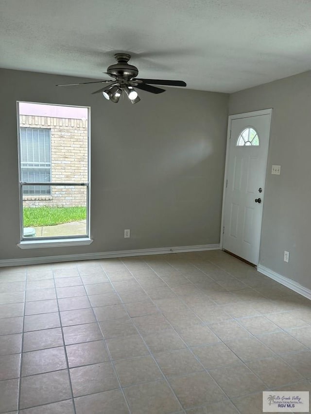 tiled entrance foyer with a ceiling fan, a textured ceiling, and baseboards