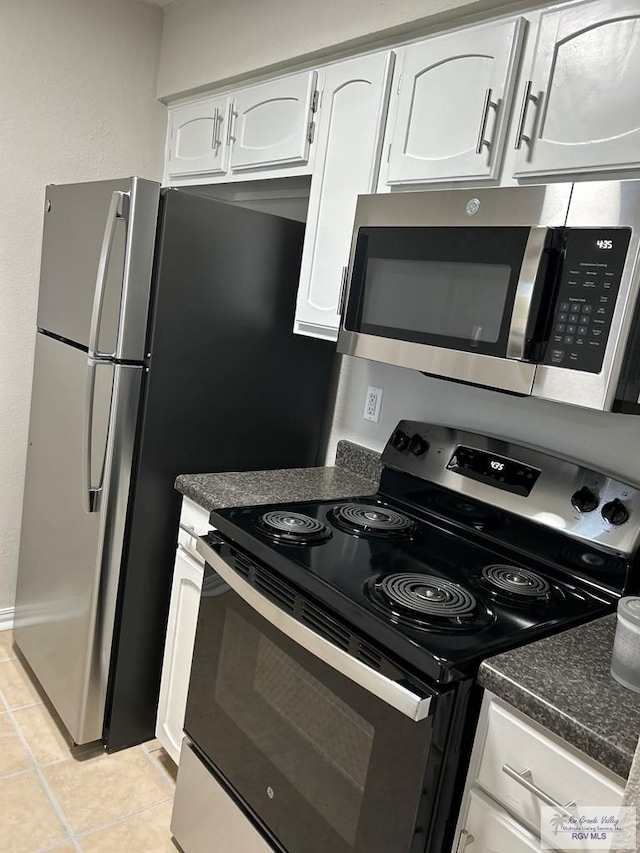 kitchen featuring stainless steel appliances, dark stone counters, white cabinetry, and light tile patterned floors