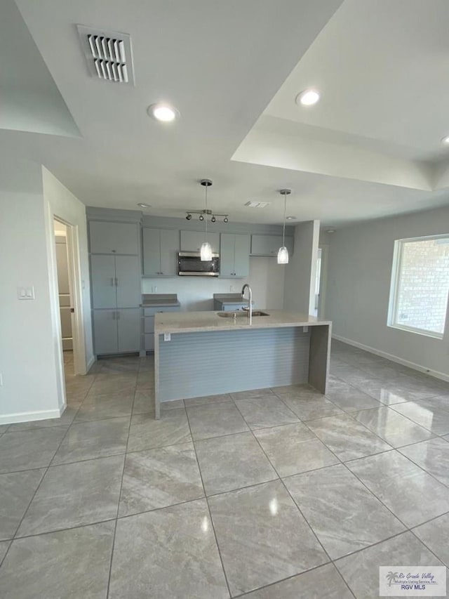 kitchen featuring gray cabinets, a kitchen island with sink, sink, and hanging light fixtures