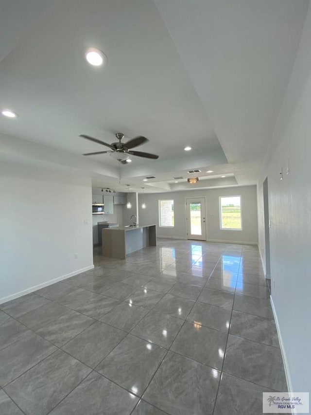 unfurnished living room with tile patterned flooring, ceiling fan, and sink