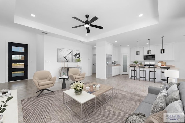 living room featuring light hardwood / wood-style floors, a raised ceiling, and ceiling fan