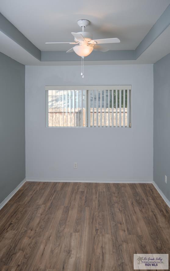 empty room with a raised ceiling, ceiling fan, and dark hardwood / wood-style flooring