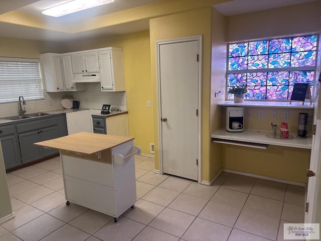 kitchen featuring a center island, sink, decorative backsplash, light tile patterned flooring, and white cabinetry