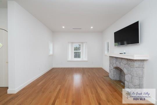 unfurnished living room featuring light wood-type flooring and a stone fireplace