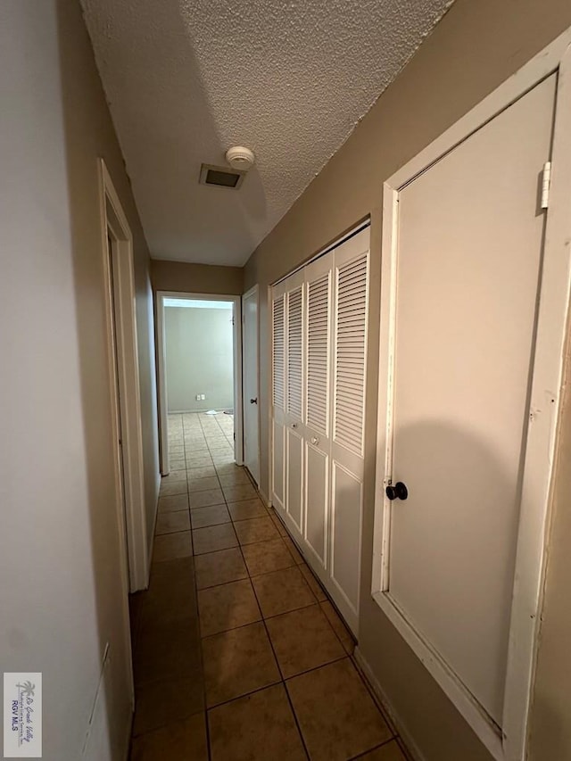 corridor with a textured ceiling and dark tile patterned floors