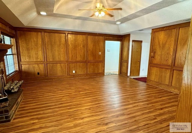 spare room with wooden walls, a tray ceiling, and light hardwood / wood-style floors