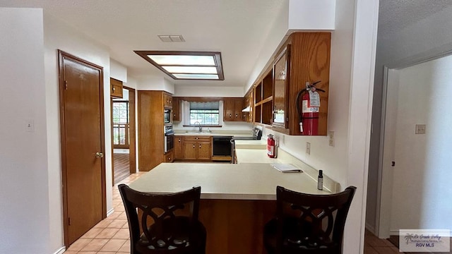 kitchen featuring a breakfast bar, sink, appliances with stainless steel finishes, light tile patterned flooring, and kitchen peninsula