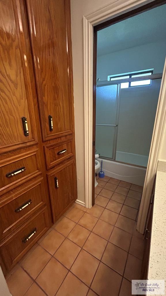 bathroom with tile patterned flooring, toilet, and combined bath / shower with glass door