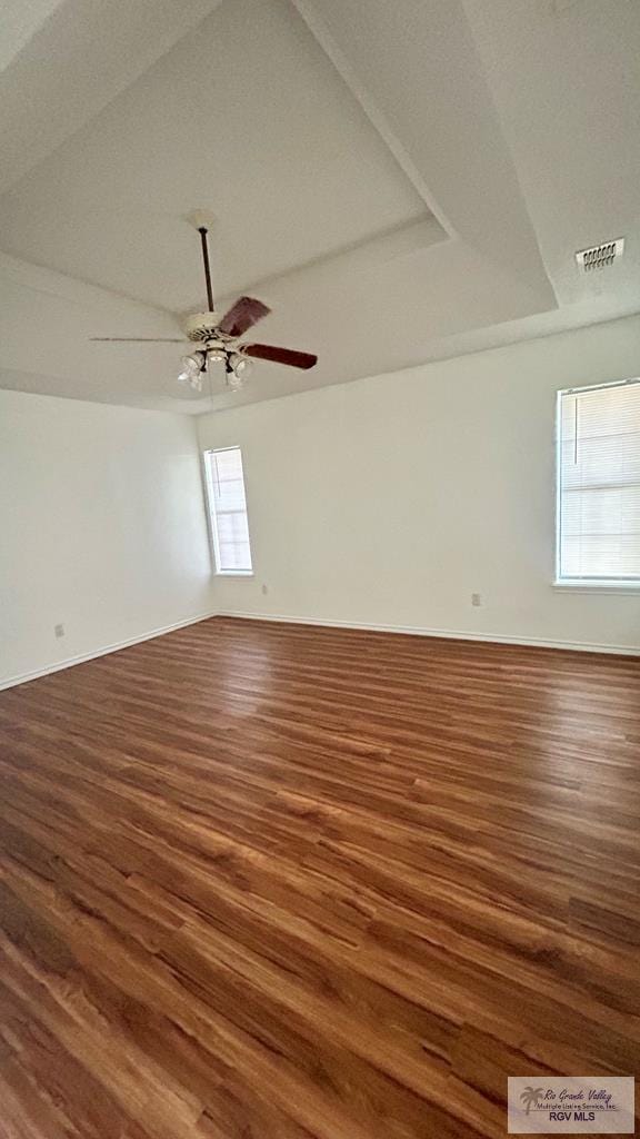 unfurnished room with ceiling fan, a raised ceiling, and dark wood-type flooring