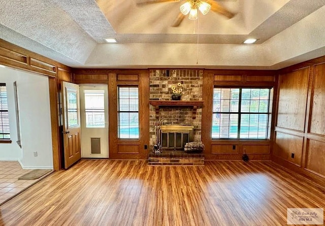 unfurnished living room featuring light wood-type flooring, a tray ceiling, a brick fireplace, and a healthy amount of sunlight