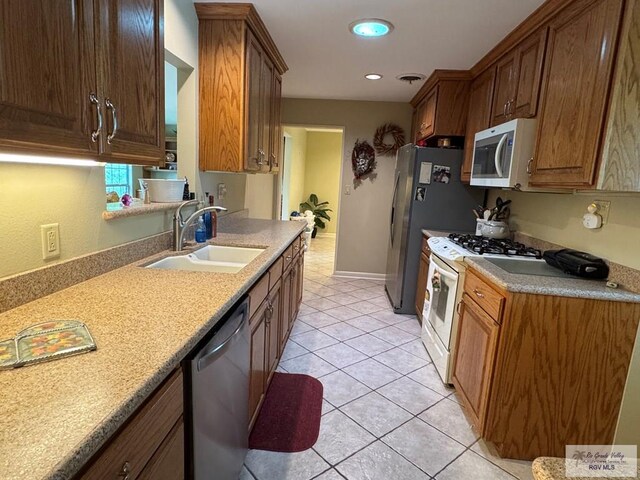kitchen with stainless steel appliances, a sink, light tile patterned flooring, light countertops, and baseboards