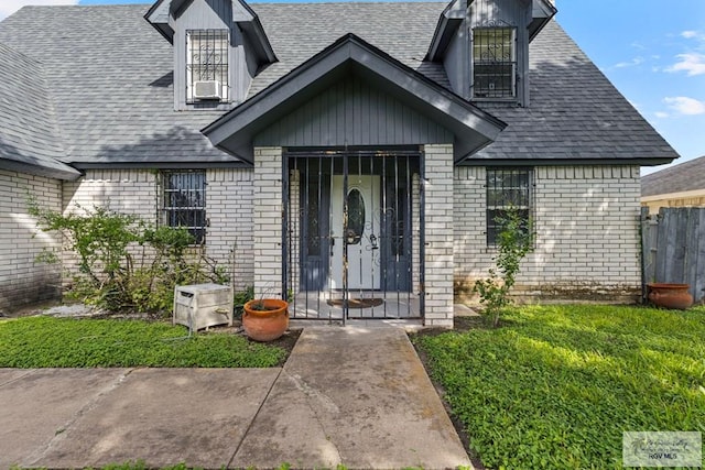 419 Mockingbird St, San Benito, TX 78586 - doorway to property featuring brick siding, a shingled roof, a lawn, and cooling unit